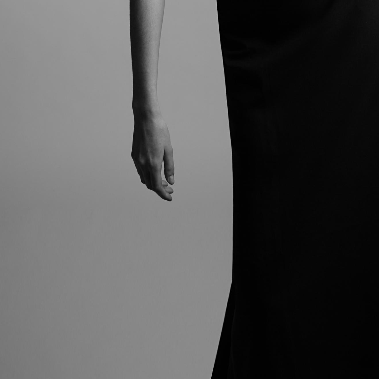 Fotografía en blanco y negro en el que destaca un antebrazo y mano femeninos, en paralelo a una gran mancha negra