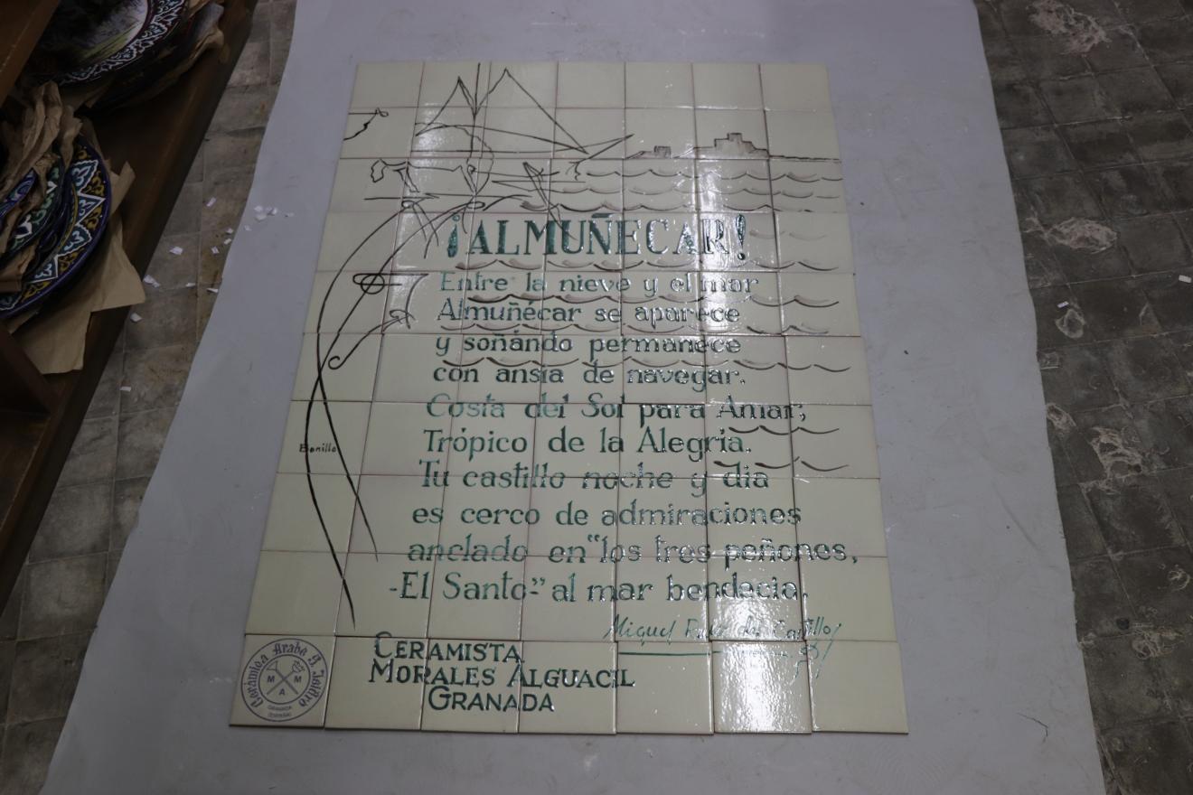 Paño de azulejos blancos con texto y un esbozo de escena marina al fondo